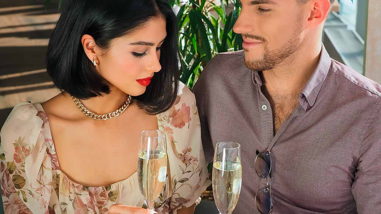 An intercultural couple on a romantic first dinner date, clinking champagne glasses.