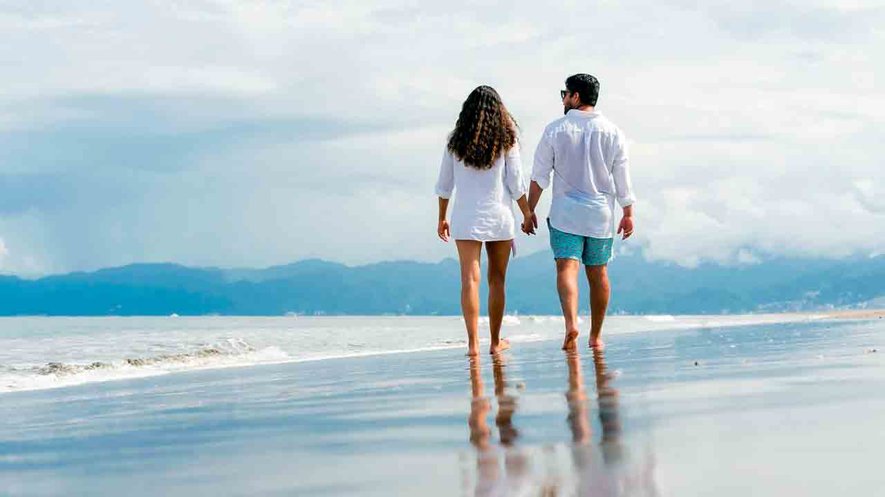 A happy Western man and a Filipina woman walking together on a beautiful Philippine beach at sunset.